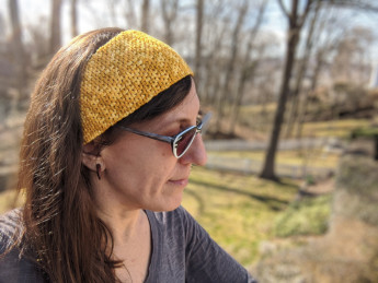 A photo of Stacy Pamela in the woods, wearing a yellow crochet headband.